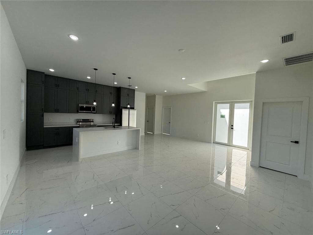 Kitchen with open floor plan, an island with sink, decorative light fixtures, stainless steel appliances, and light marble finish floors
