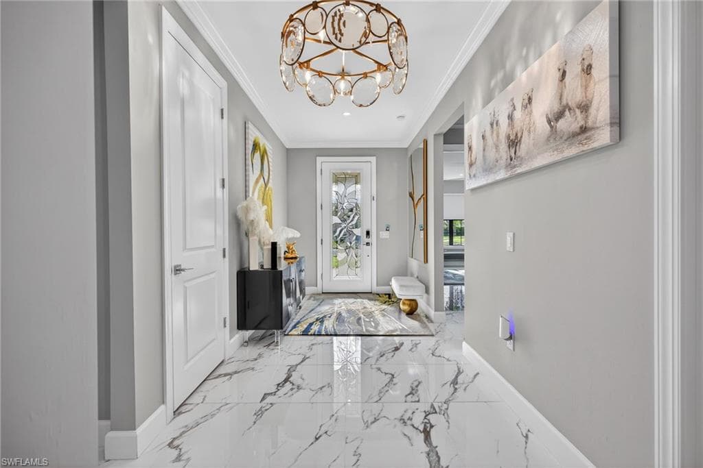 Foyer entrance with a chandelier, ornamental molding, and marble tiled flooring