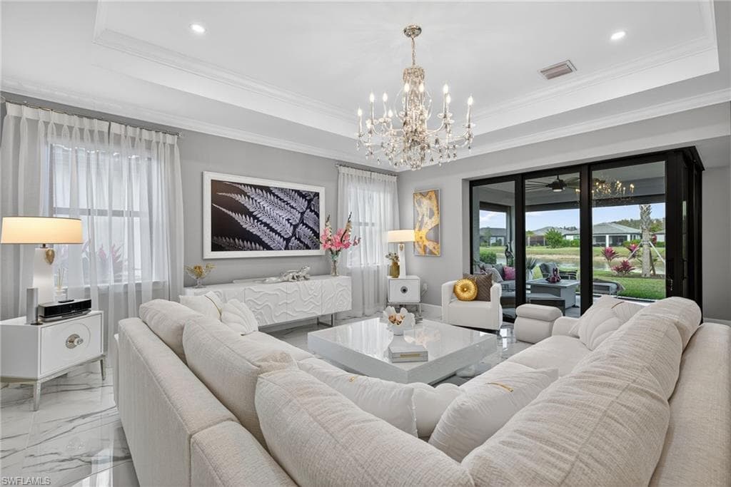 Living area with plenty of natural light, a tray ceiling, a chandelier, marble finish floors, and ornamental molding