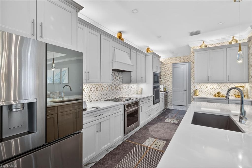 Kitchen featuring decorative light fixtures, stainless steel appliances, light stone countertops, crown molding, and premium range hood