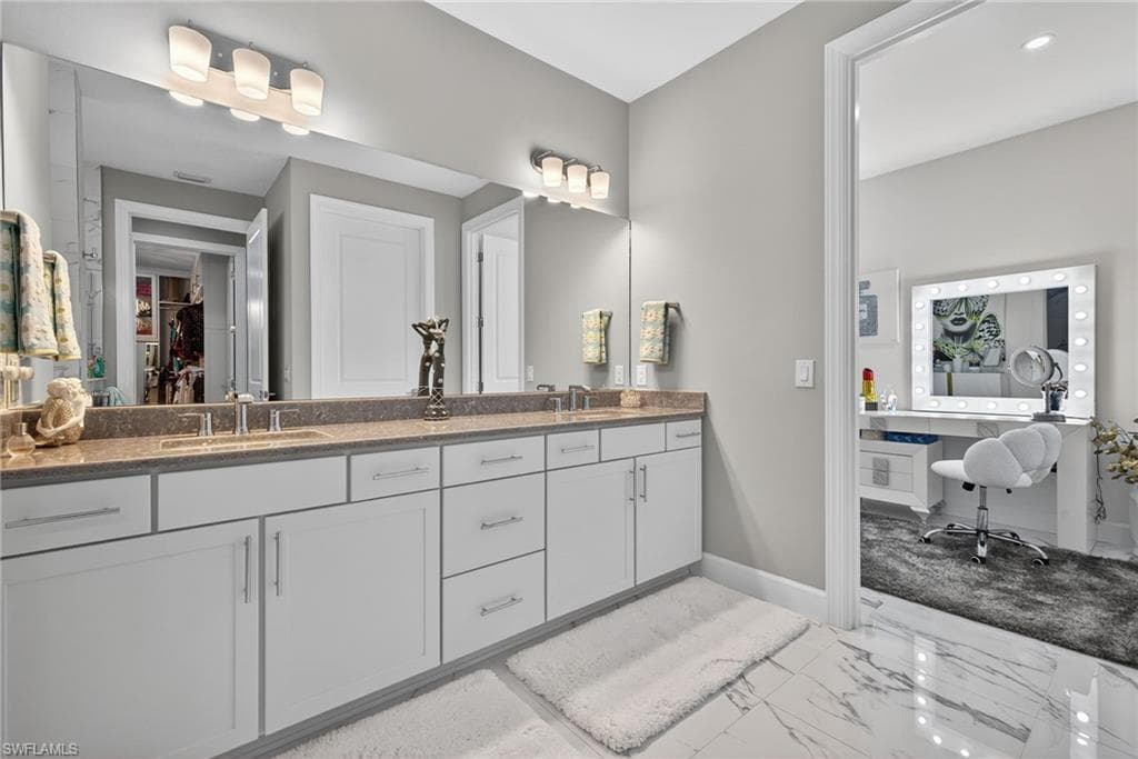 Bathroom with double vanity, light marble finish floors, and a walk in closet