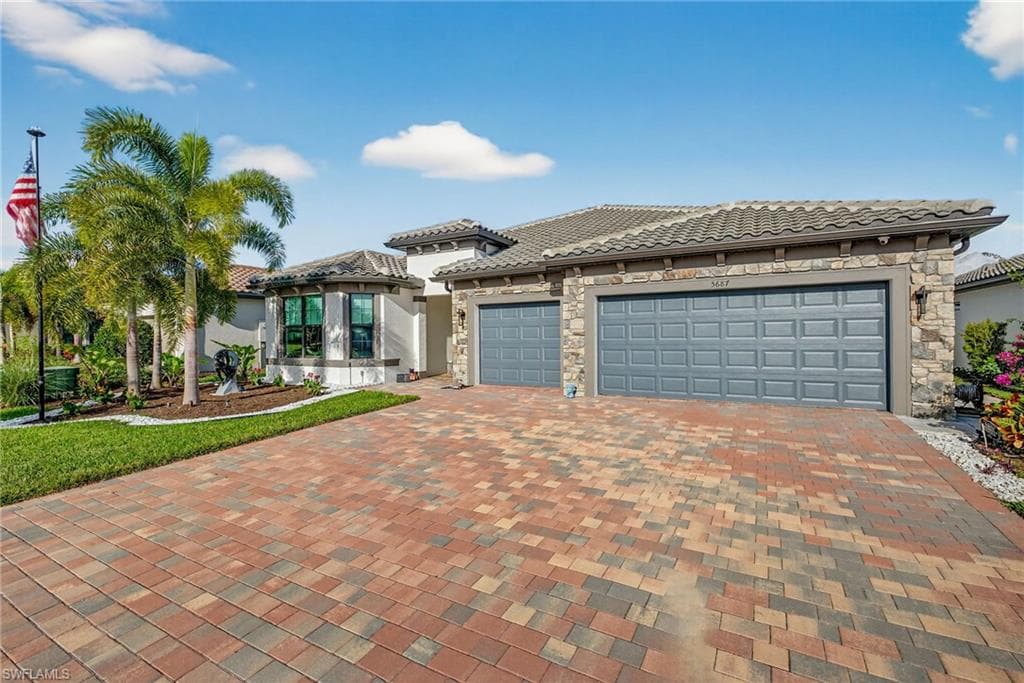View of front facade featuring a tiled roof, stone siding, driveway, and a garage