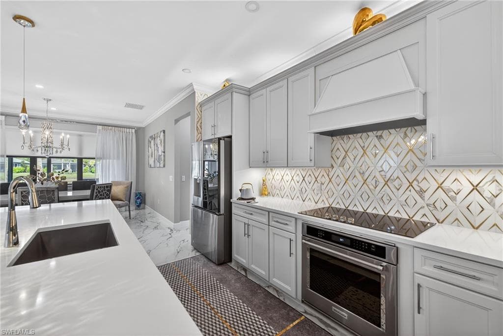 Kitchen featuring stainless steel appliances, crown molding, custom range hood, light stone counters, and pendant lighting