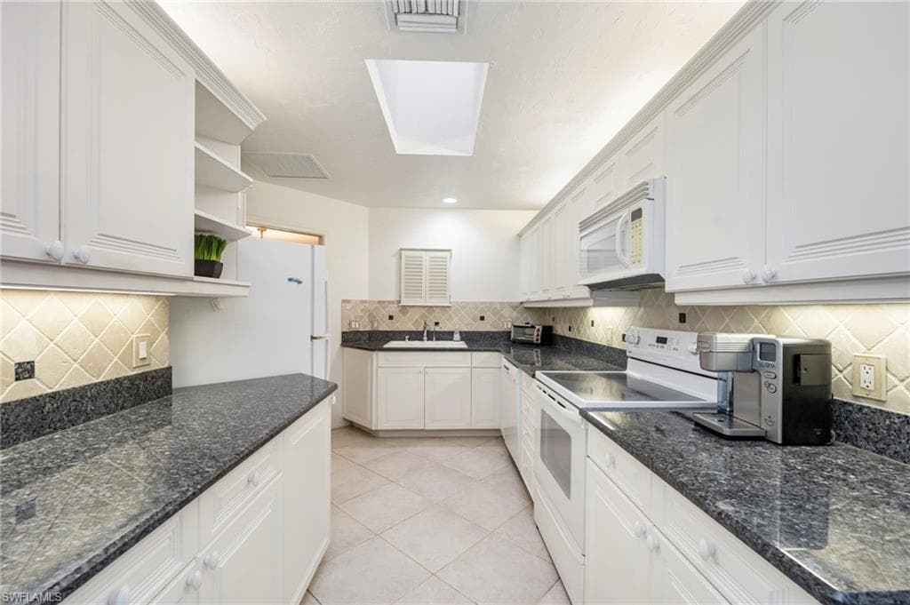 Kitchen featuring white appliances, open shelves, white cabinets, light tile patterned floors, and tasteful backsplash