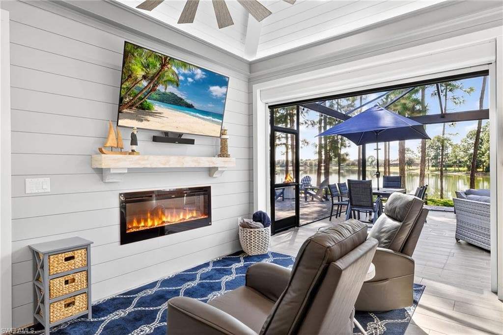 Living area with a sunroom, a glass covered fireplace, plenty of natural light, ceiling fan, and wood walls