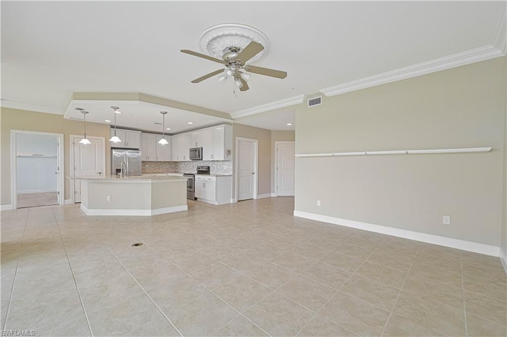 Open-concept living area featuring large format tile flooring, crown molding, and a kitchen with white cabinetry