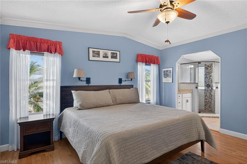 Primary Bedroom featuring a textured ceiling, ornamental molding, arched walkways, light wood finished floors, and ceiling fan