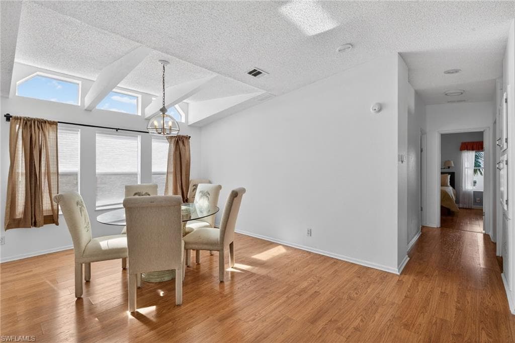Dining area featuring light wood-type flooring, vaulted ceiling, and a textured ceiling