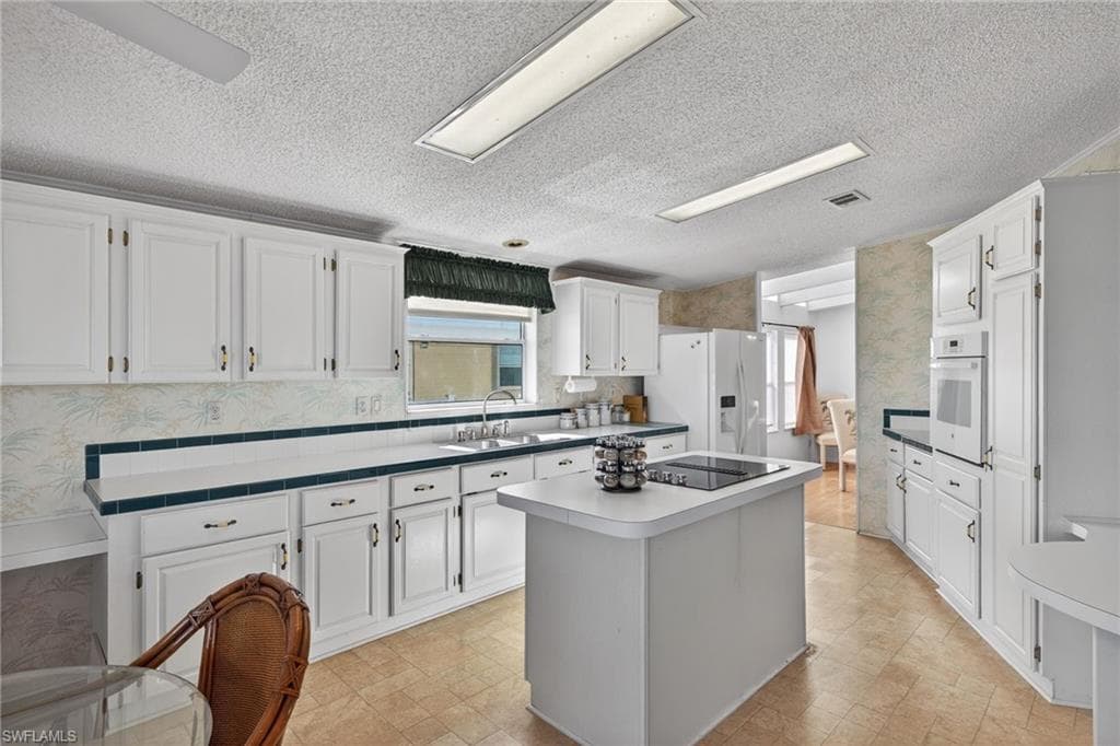 Kitchen with wallpapered walls, a center island, a textured ceiling, white cabinetry, and white appliances