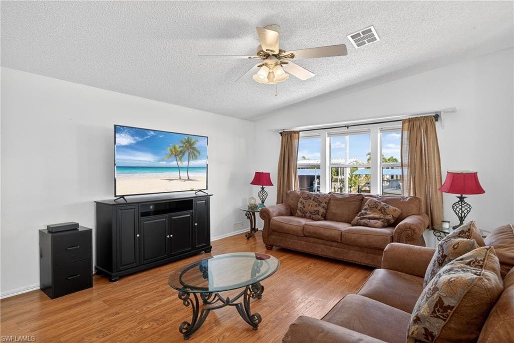 Family room with lofted ceiling, light wood-type flooring, a ceiling fan, and a textured ceiling