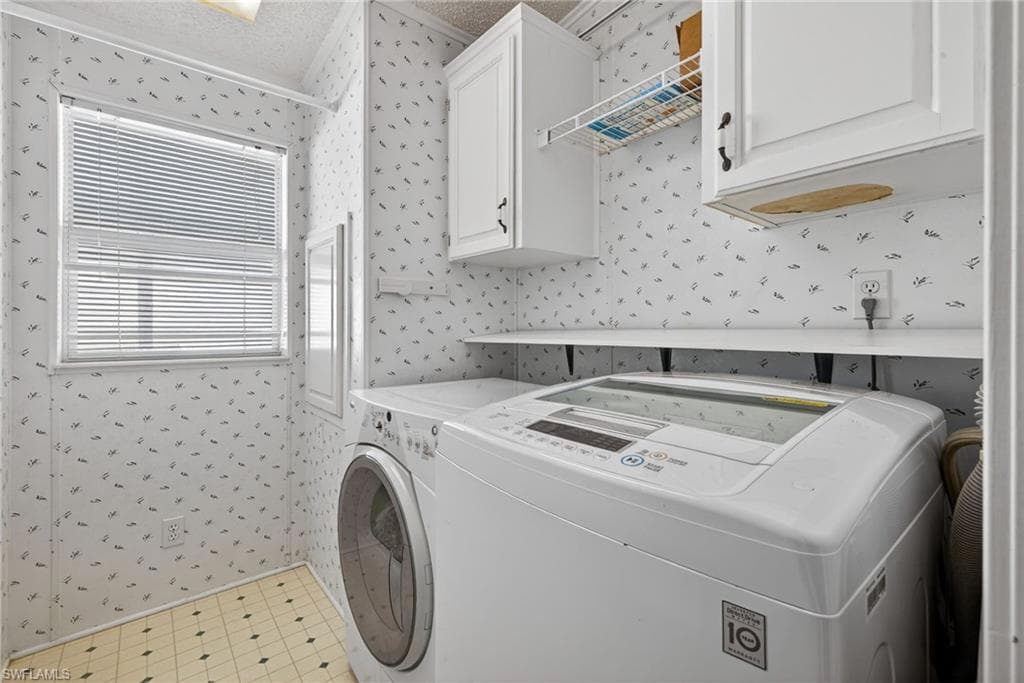 Washroom featuring wallpapered walls, cabinet space, and independent washer and dryer