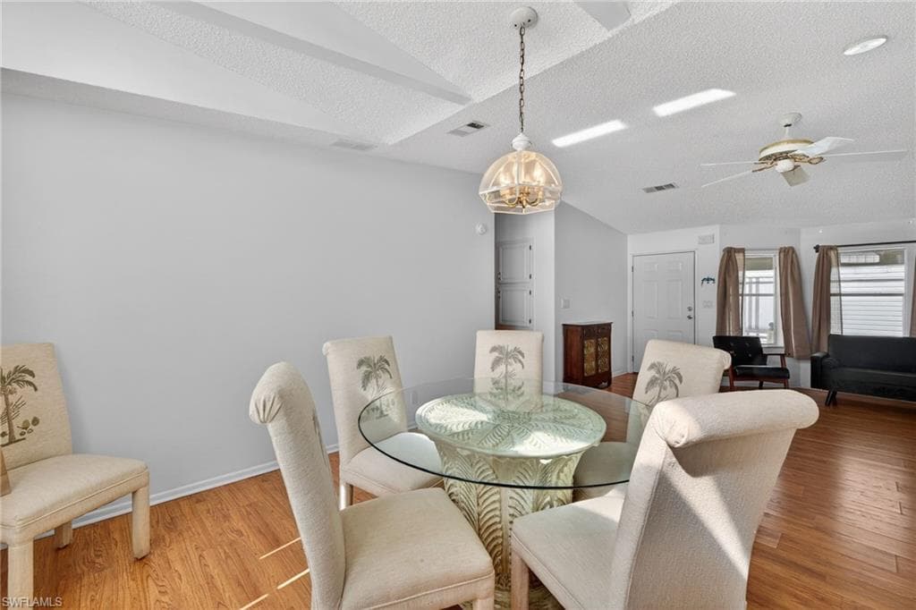 Dining area featuring lofted ceiling, wood finished floors, a chandelier, a textured ceiling, and ceiling fan