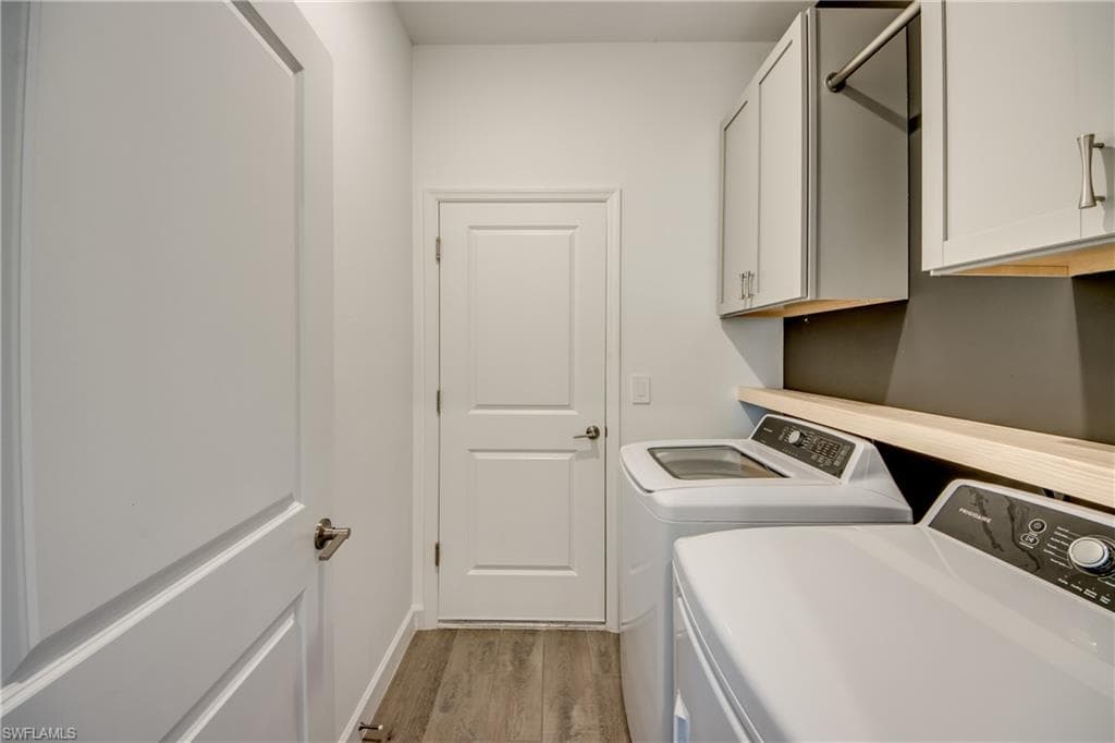 Washroom with light wood finished floors, washer and clothes dryer, and cabinet space