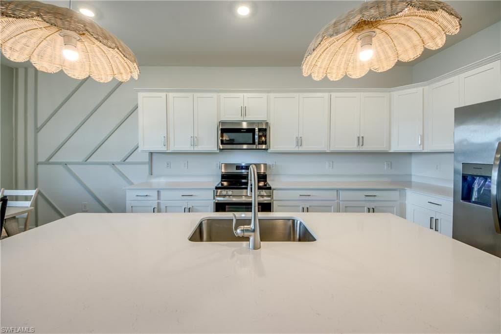 Kitchen with white cabinets, appliances with stainless steel finishes, pendant lighting, and light stone countertops