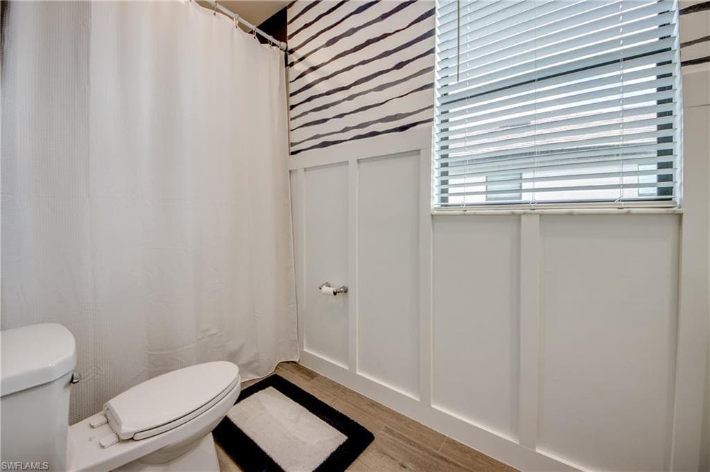 Bathroom featuring curtained shower, a decorative wall, and light wood-style flooring