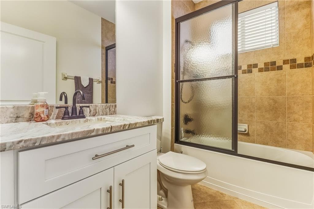 Full bathroom featuring vanity, shower / bath combination with glass door, and light tile patterned flooring