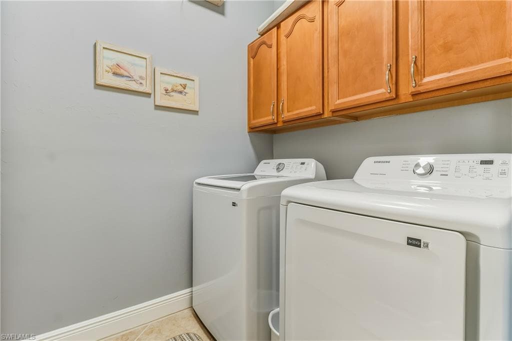 Laundry area featuring washing machine and clothes dryer, cabinet space, and light tile patterned floors
