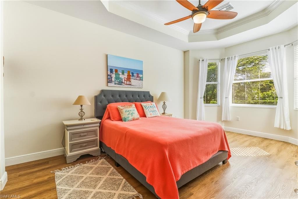 Bedroom featuring wood finished floors, ornamental molding, a tray ceiling, and ceiling fan