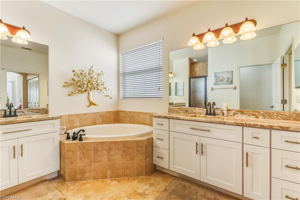 Full bath featuring two vanities, a garden tub, a shower stall, and light tile patterned flooring
