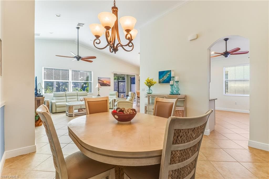 Dining space with ceiling fan, a chandelier, light tile patterned floors, and high vaulted ceiling
