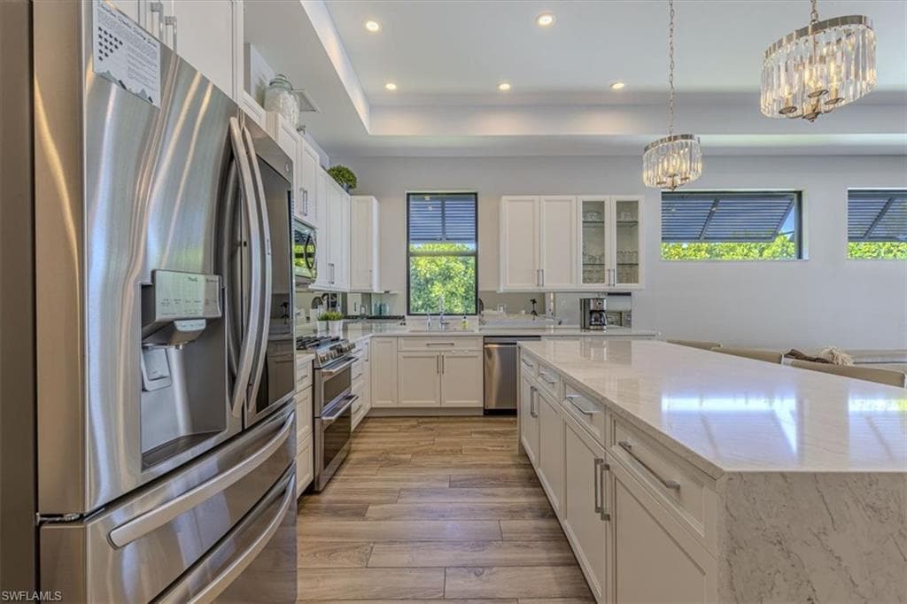 Kitchen featuring stainless steel appliances, glass insert cabinets, white cabinetry, recessed lighting, and light stone counters