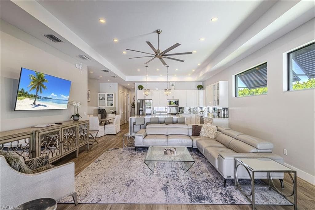 Living area with a tray ceiling, dark wood-type flooring, plenty of natural light, and recessed lighting
