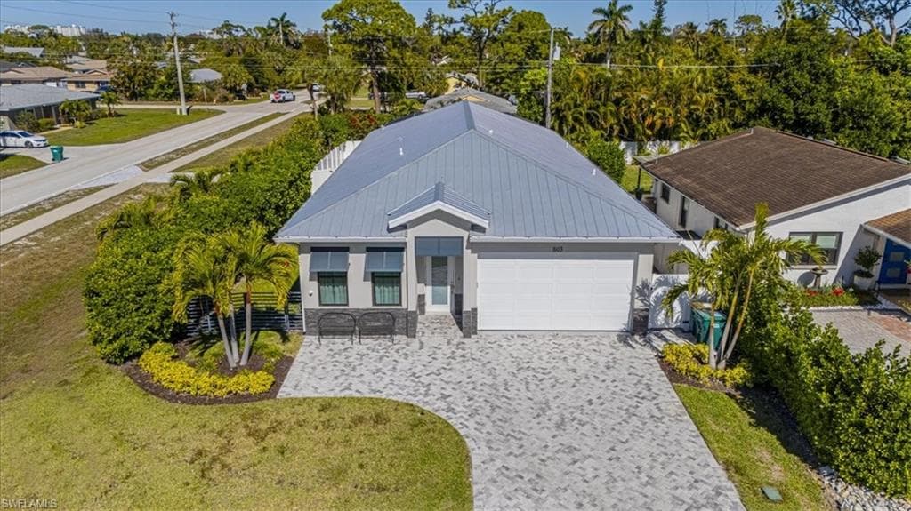 Ranch-style house featuring decorative driveway, a garage, a front lawn, a metal roof, and view of scattered trees