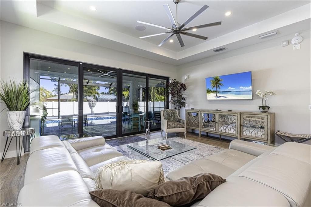 Living room with a raised ceiling, wood finished floors, and ceiling fan