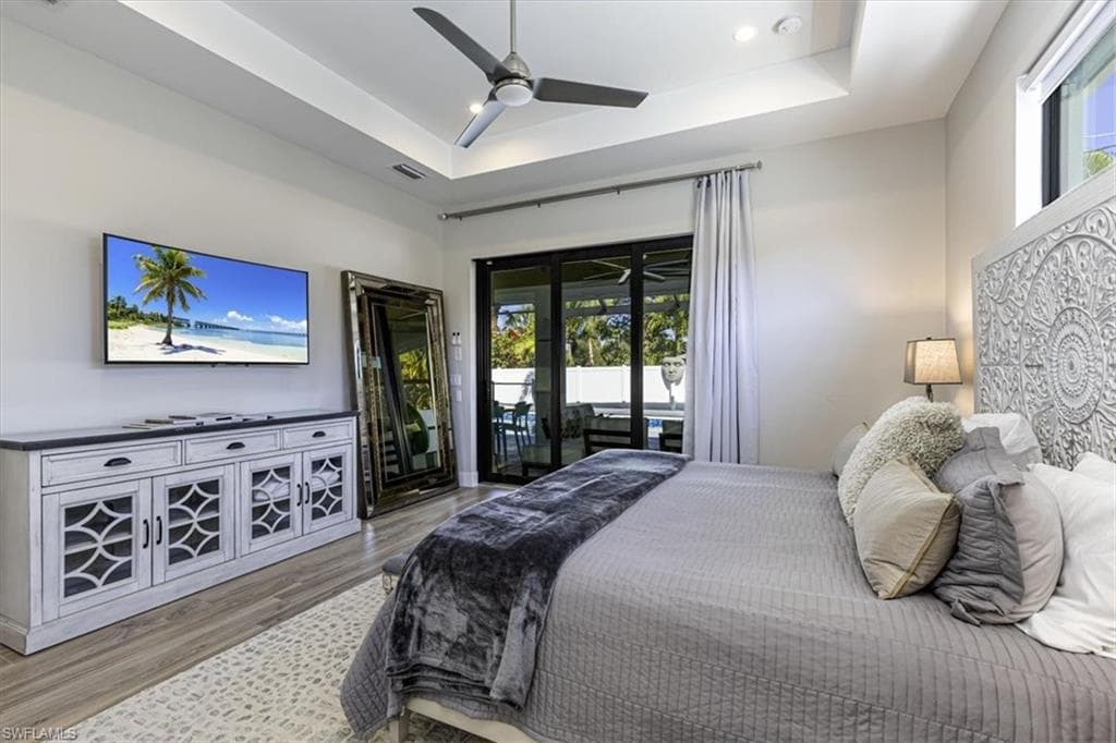 Bedroom featuring access to exterior, ceiling fan, a tray ceiling, wood finished floors, and recessed lighting
