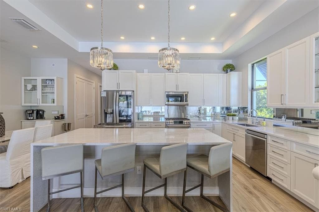 Kitchen featuring glass insert cabinets, a tray ceiling, white cabinetry, a kitchen breakfast bar, and a kitchen island
