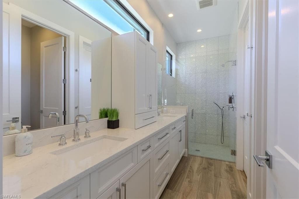 Bathroom featuring double vanity, a stall shower, light wood finished floors, and recessed lighting