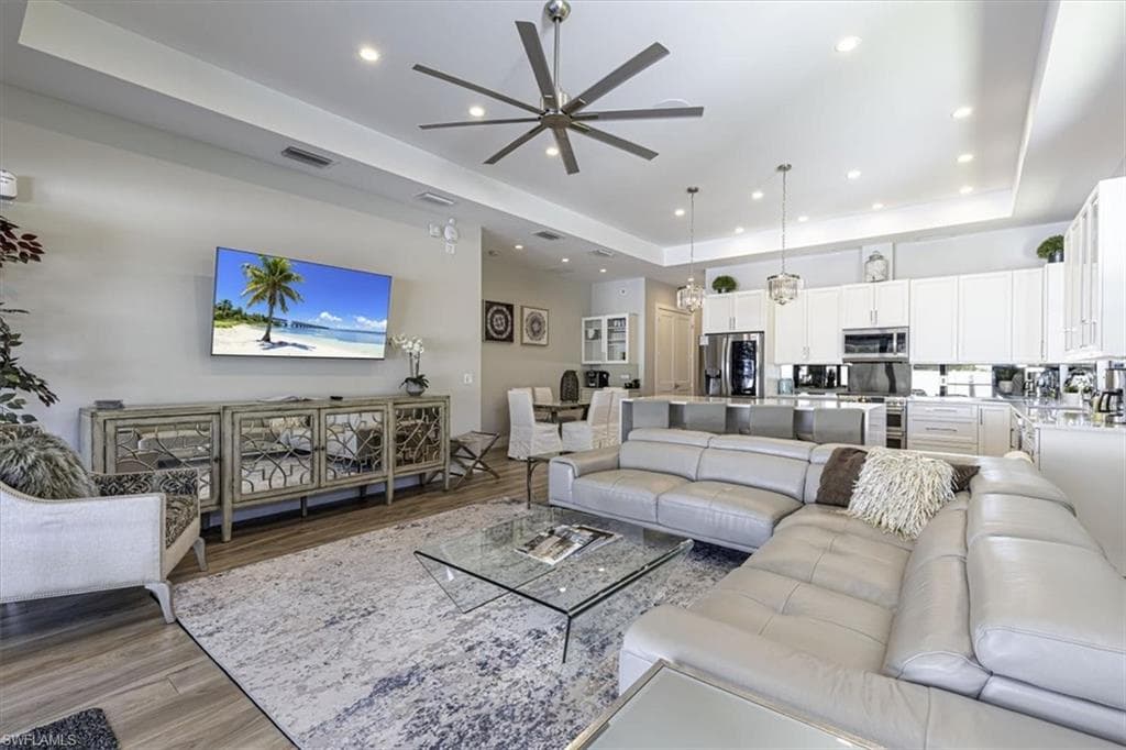 Living area with a tray ceiling, light wood-style flooring, a ceiling fan, and recessed lighting
