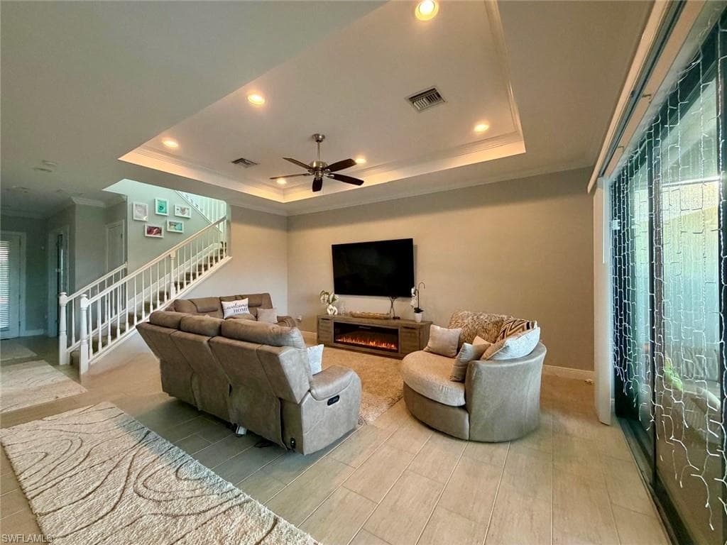 Living room with crown molding, recessed lighting, ceiling fan, stairs, and a warm lit fireplace