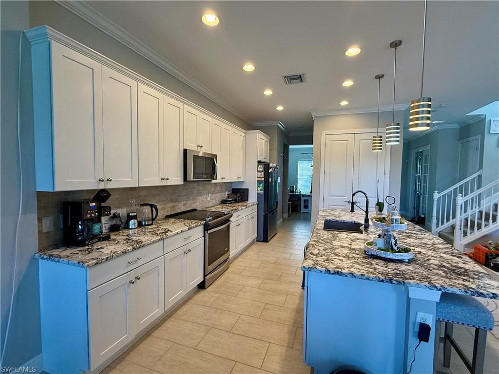 Kitchen with appliances with stainless steel finishes, a kitchen bar, a center island with sink, white cabinetry, and light stone counters