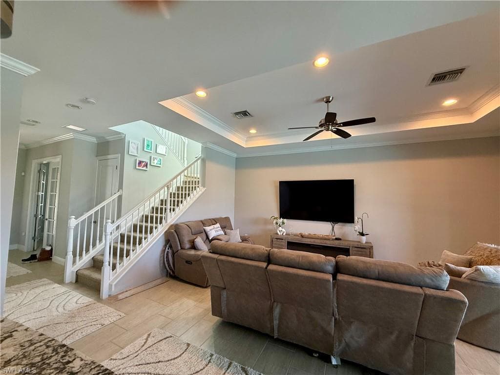 Living room with crown molding, light wood-style flooring, stairway, recessed lighting, and a tray ceiling