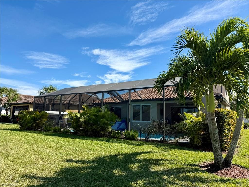 Rear view of property with a lanai, a sunroom, a lawn, and stucco siding