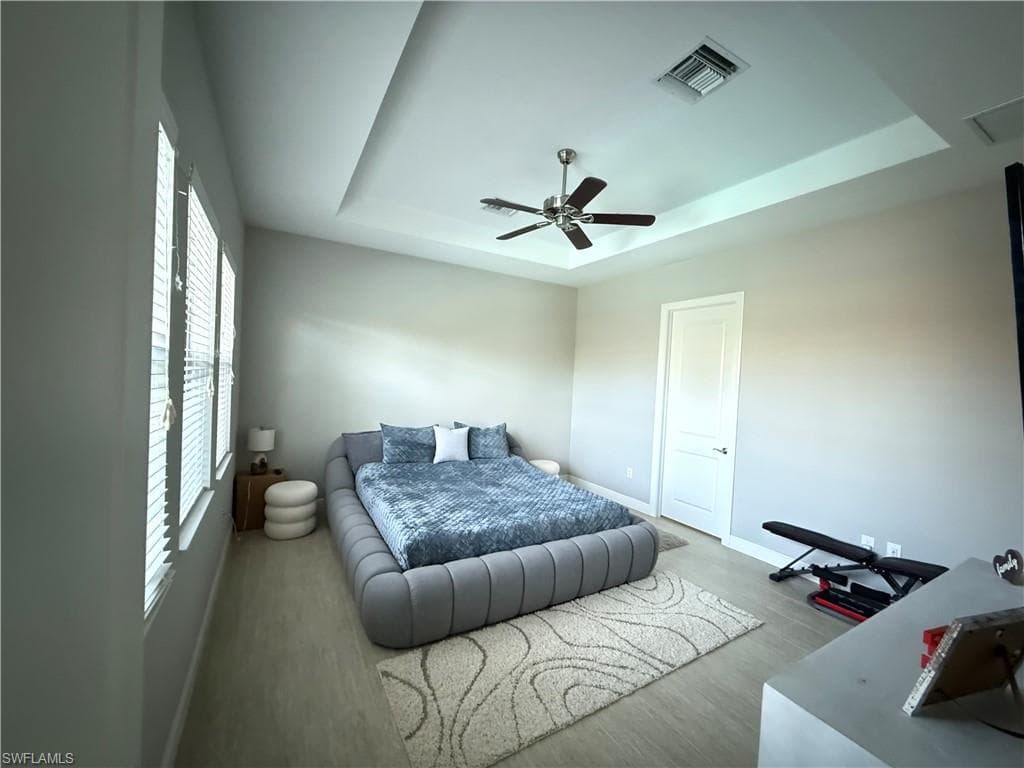Bedroom with a tray ceiling, wood finished floors, and ceiling fan