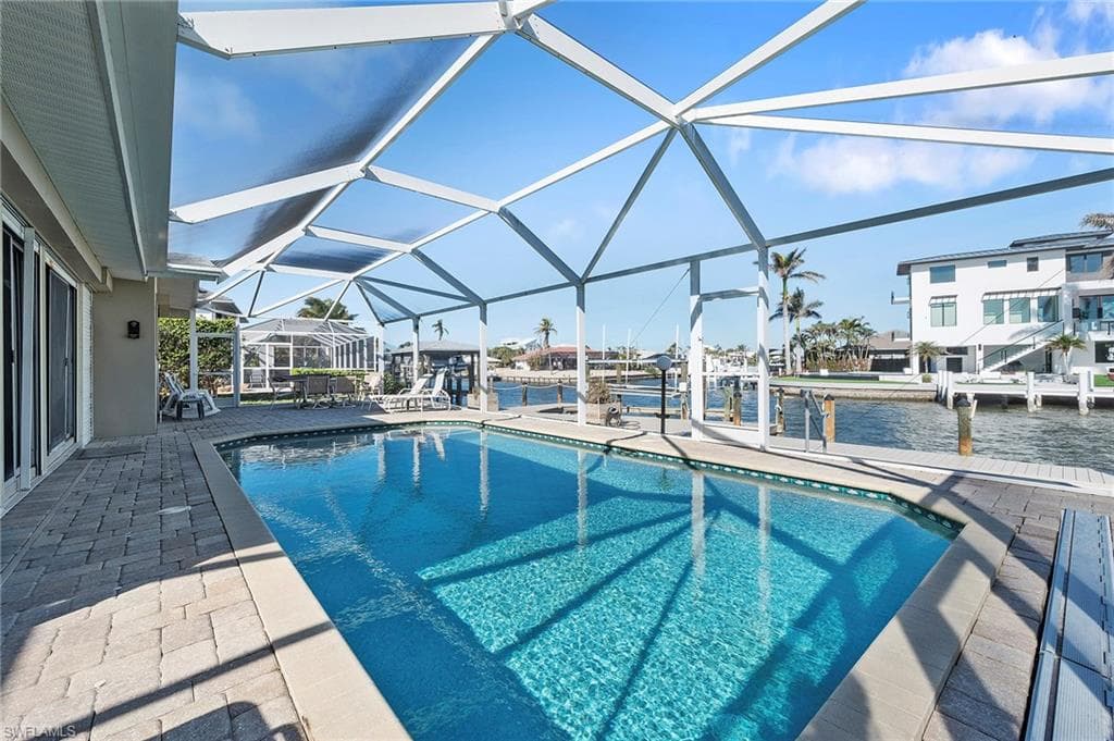 View of swimming pool featuring canal view, a dock, a patio area, and a lanai