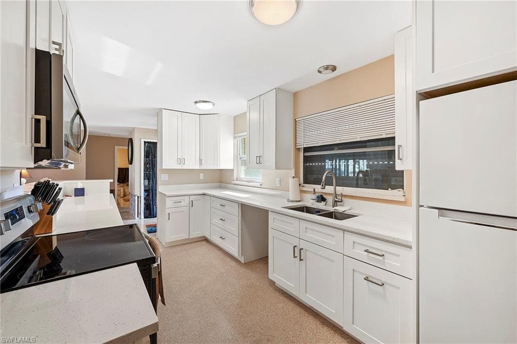Kitchen featuring light carpet, sink, white cabinets, and appliances with stainless steel finishes