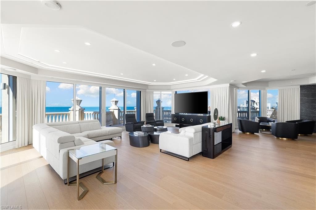 Living area featuring floor to ceiling windows, a raised ceiling, light wood-style floors, and recessed lighting