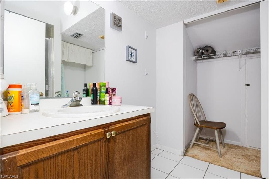 Full bathroom with vanity, a textured ceiling, light tile patterned flooring, and a spacious closet