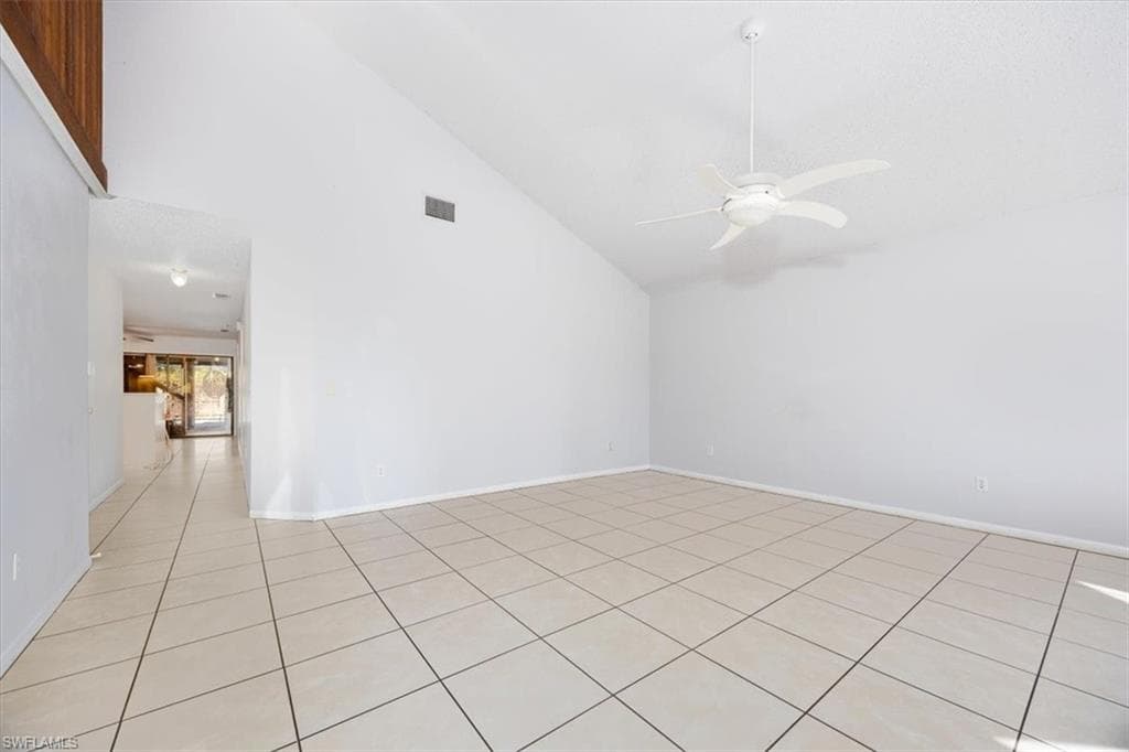 Empty room featuring ceiling fan, lofted ceiling, and light tile patterned floors
