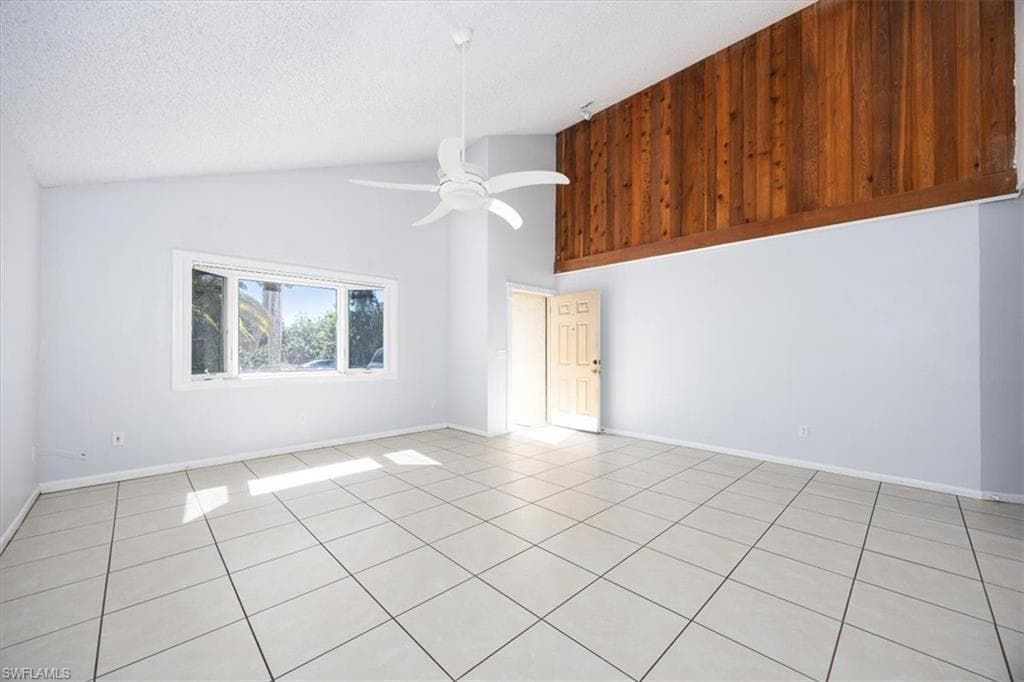 Unfurnished room with ceiling fan, light tile patterned floors, and a high textured ceiling