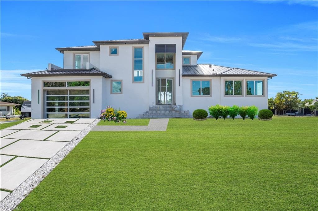 Back of house with a standing seam roof, concrete driveway, a lawn, and an attached garage