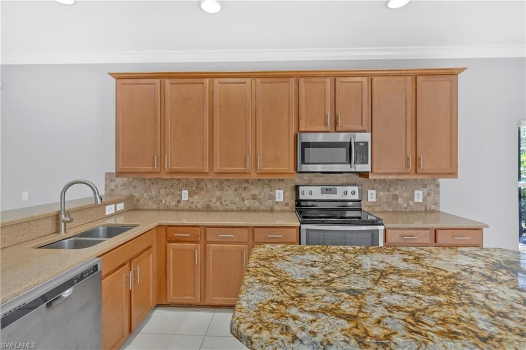 Kitchen featuring stainless steel appliances, light stone counters, tasteful backsplash, light tile patterned flooring, and crown molding