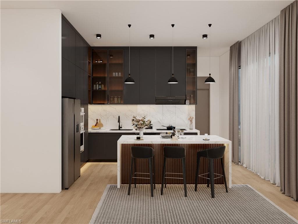 Kitchen featuring modern cabinets, a breakfast bar area, stainless steel appliances, and decorative light fixtures (Rendered photo)