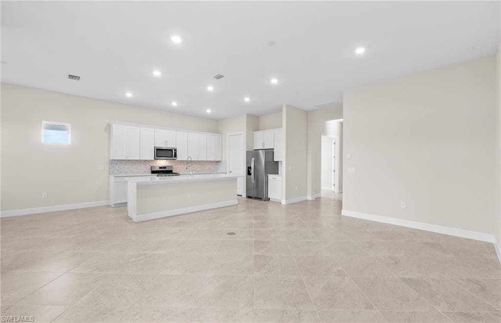 Kitchen with white cabinets, open floor plan, stainless steel appliances, a kitchen island with sink, and backsplash