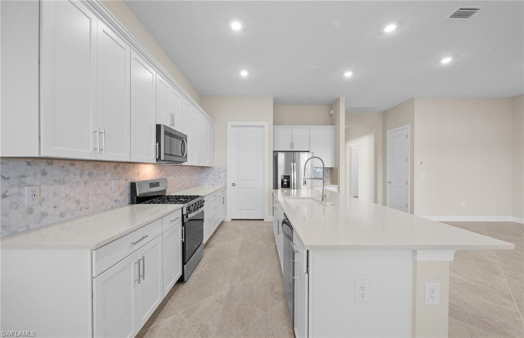 Kitchen with stainless steel appliances, white cabinetry, recessed lighting, a center island with sink, and tasteful backsplash
