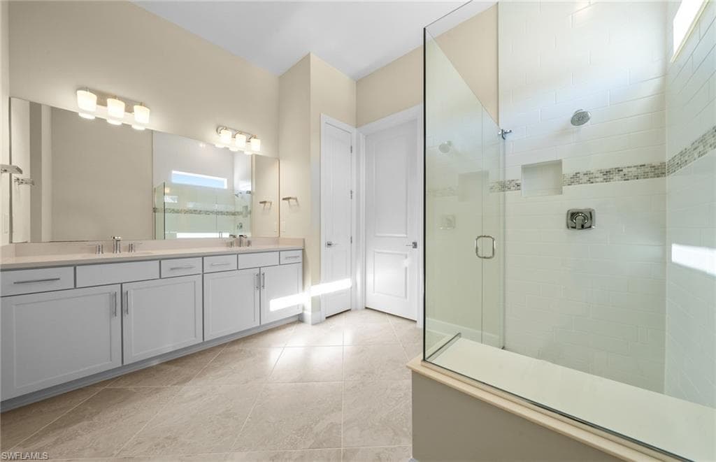 Full bath with a shower stall, double vanity, and light tile patterned floors