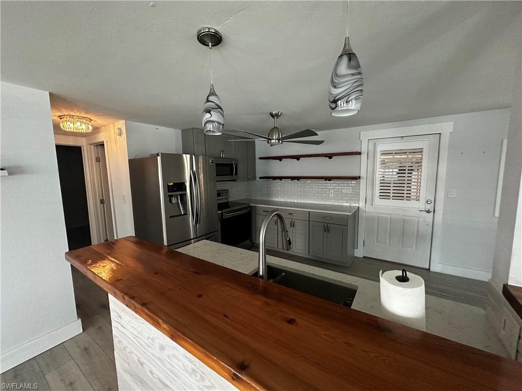 Kitchen with pendant lighting, stainless steel appliances, wooden counters, and gray cabinets